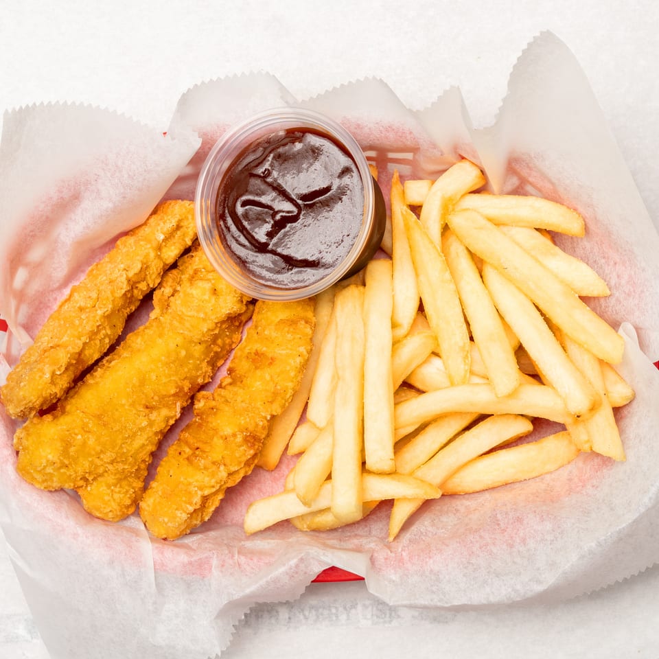 Basket of golden fried chicken tenders and French fries served with a cup of dark dipping sauce.