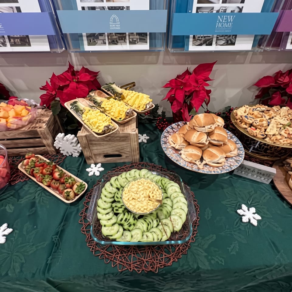 Festive buffet table featuring sliders, macaroni salad, cucumber slices, fruit skewers, cookies, poinsettias, and snowflake decorations.