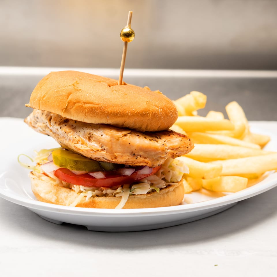 Grilled chicken sandwich with lettuce, tomato, onion, and pickles served with fries on a white plate.