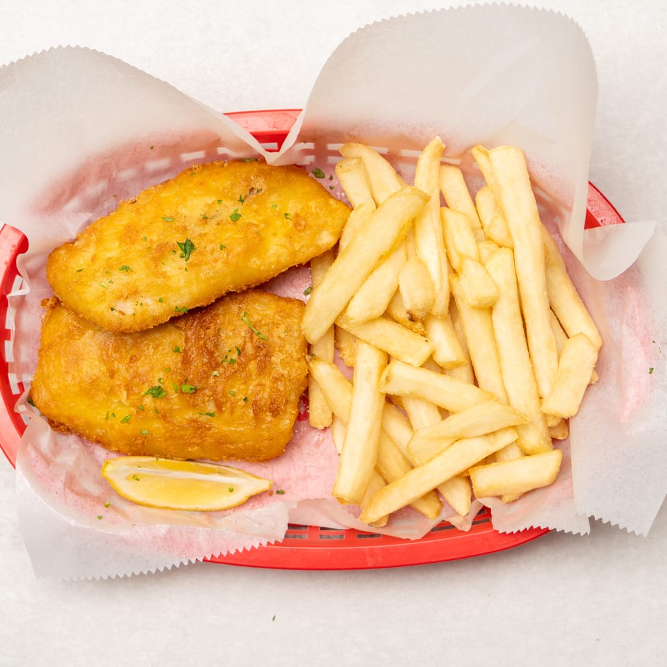 Golden fried fish fillets with French fries and a lemon wedge in a red paper-lined basket.