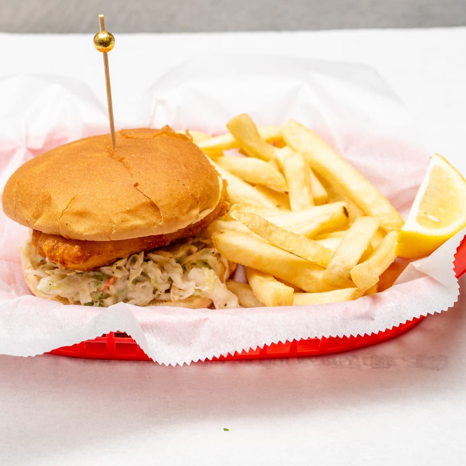 Crispy chicken sandwich with creamy slaw, fries, and a lemon wedge served on a red paper-lined tray.