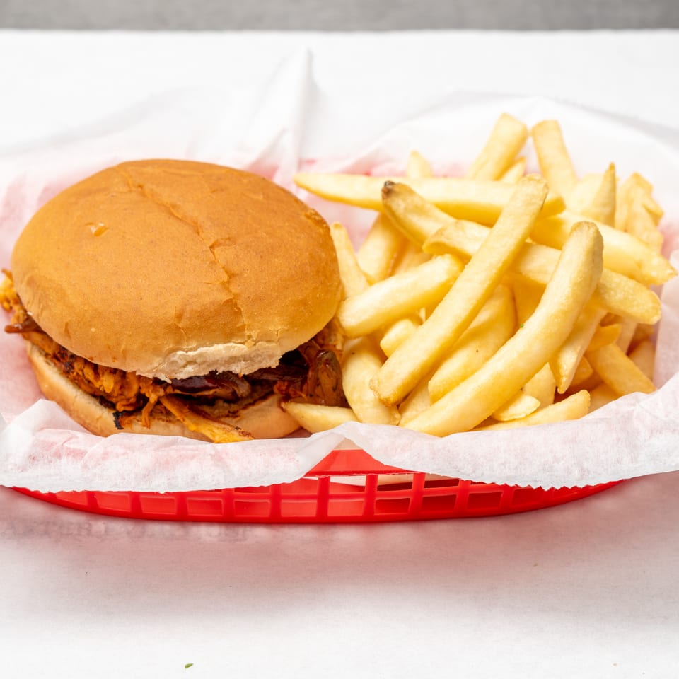 Pulled pork sandwich on a toasted bun served with golden French fries in a red plastic basket.