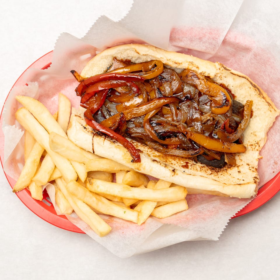 Grilled steak sandwich topped with sautéed peppers and onions, served with golden French fries on a red tray.