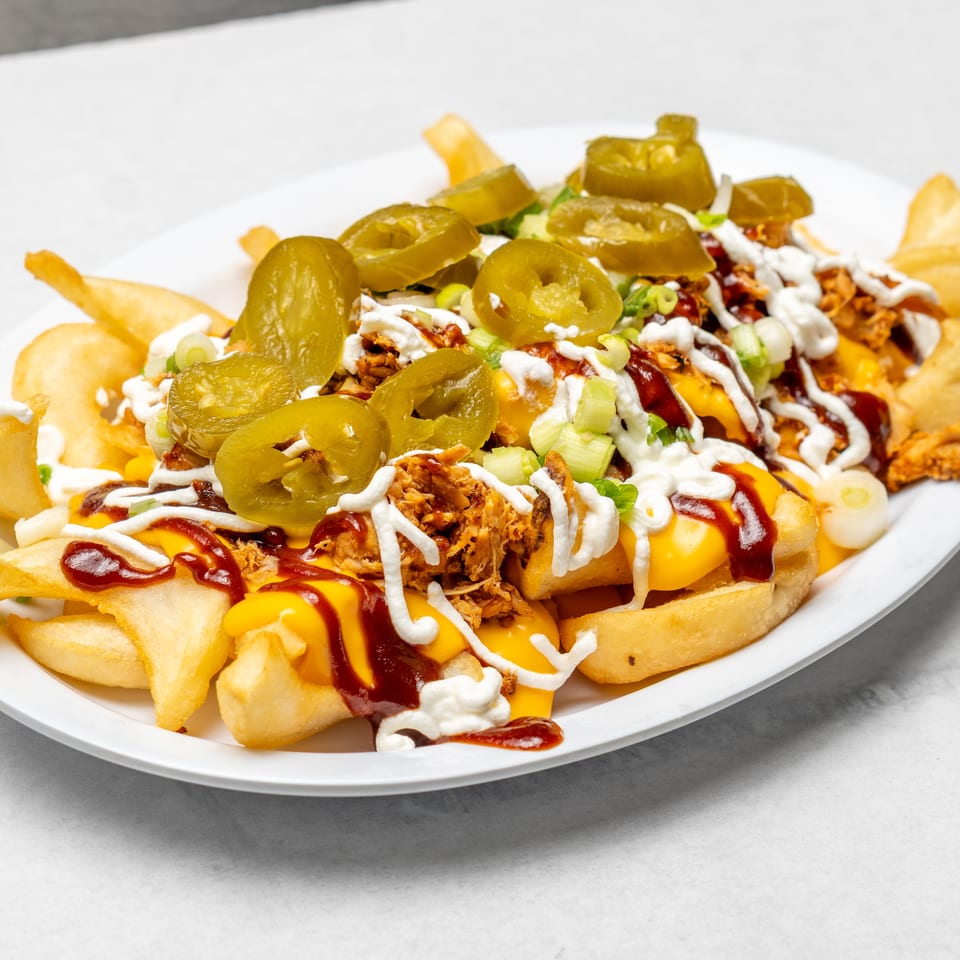 Loaded fries topped with shredded meat, melted cheese, jalapeños, green onions, ketchup, and white sauce on a plate.