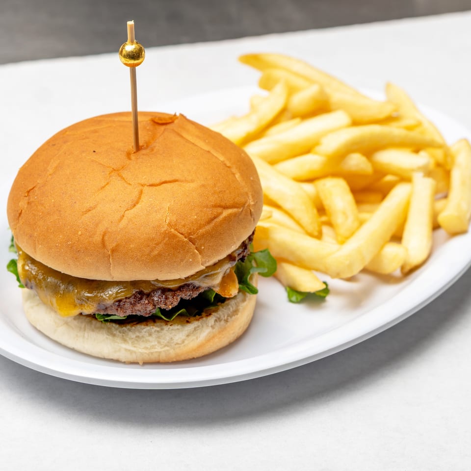 Cheeseburger with lettuce on a toasted bun, secured with a skewer, served alongside golden French fries on a white plate.