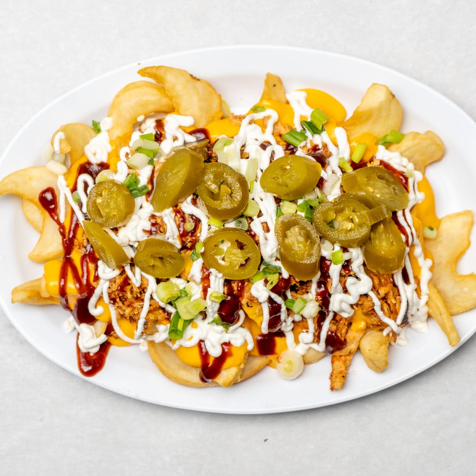 Loaded plate of fries topped with cheese, barbecue sauce, ranch dressing, shredded meat, jalapeños, and green onions.